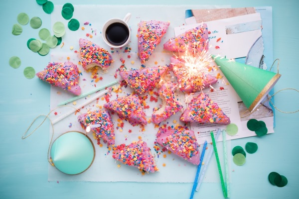 A festive table setting with sparkler-adorned pastries, confetti, a cup of coffee, and party decorations.