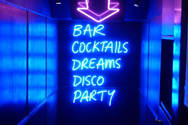 Neon signs inside a venue indicating "bar cocktails dreams disco party".