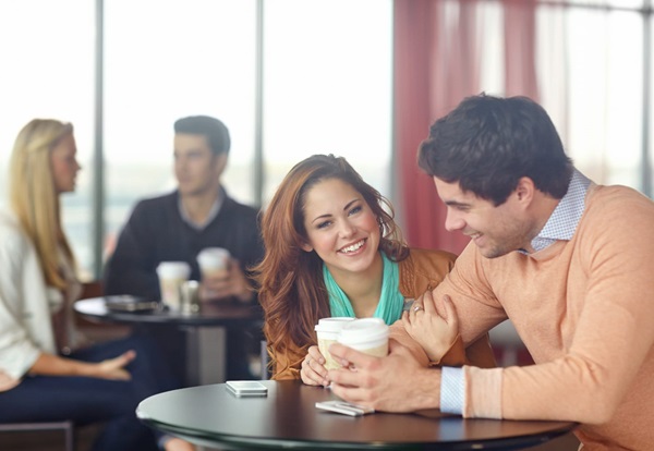 Two people smiling and enjoying a conversation over coffee, with others in the background.