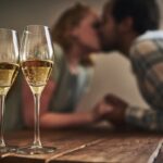 Two champagne glasses on a table, capturing a romantic moment from one of the fun date ideas in Charlotte, with a couple kissing in the background.