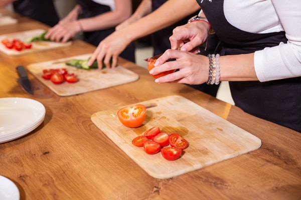 People preparing food by slicing tomatoes on cutting boards.